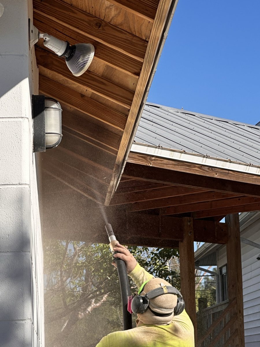 Operator blasting a wood ceiling, media spray flying